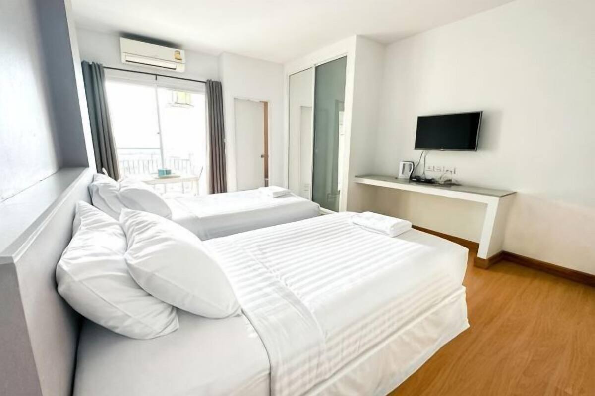 A hotel room with two beds, a TV, a desk, and a balcony.