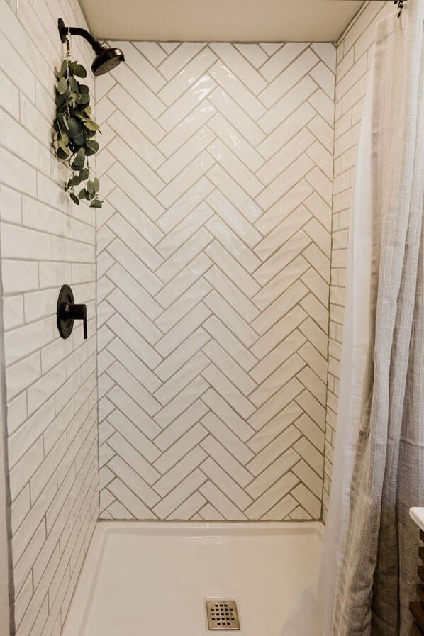A shower with a herringbone tile pattern, a showerhead, and a drain. - Beautiful Spearfish Tiny House (Spearfish)