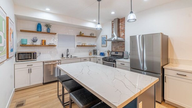 A modern kitchen with a marble island, stainless steel appliances, and wooden bar stools. - Luxury 4-bed home in Riverside Heights! (Reno)