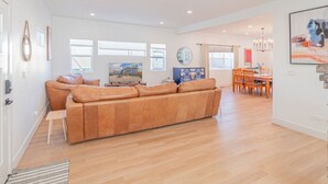 A spacious living area with a large beige sofa, a dining table with chairs, and a TV. - Luxury 4-bed home in Riverside Heights! (Reno)