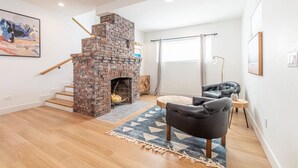 A modern living room with a brick fireplace, a staircase, a black leather sofa, and a rug. - Luxury 4-bed home in Riverside Heights! (Reno)