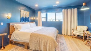 A bedroom with a large bed, a chair, a hanging light fixture, and a window with curtains. - Luxury 4-bed home in Riverside Heights! (Reno)