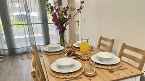 Una mesa de desayuno preparada con platos blancos, un jarro de vidrio con jugo de naranja, un florero con flores y una silla de madera.