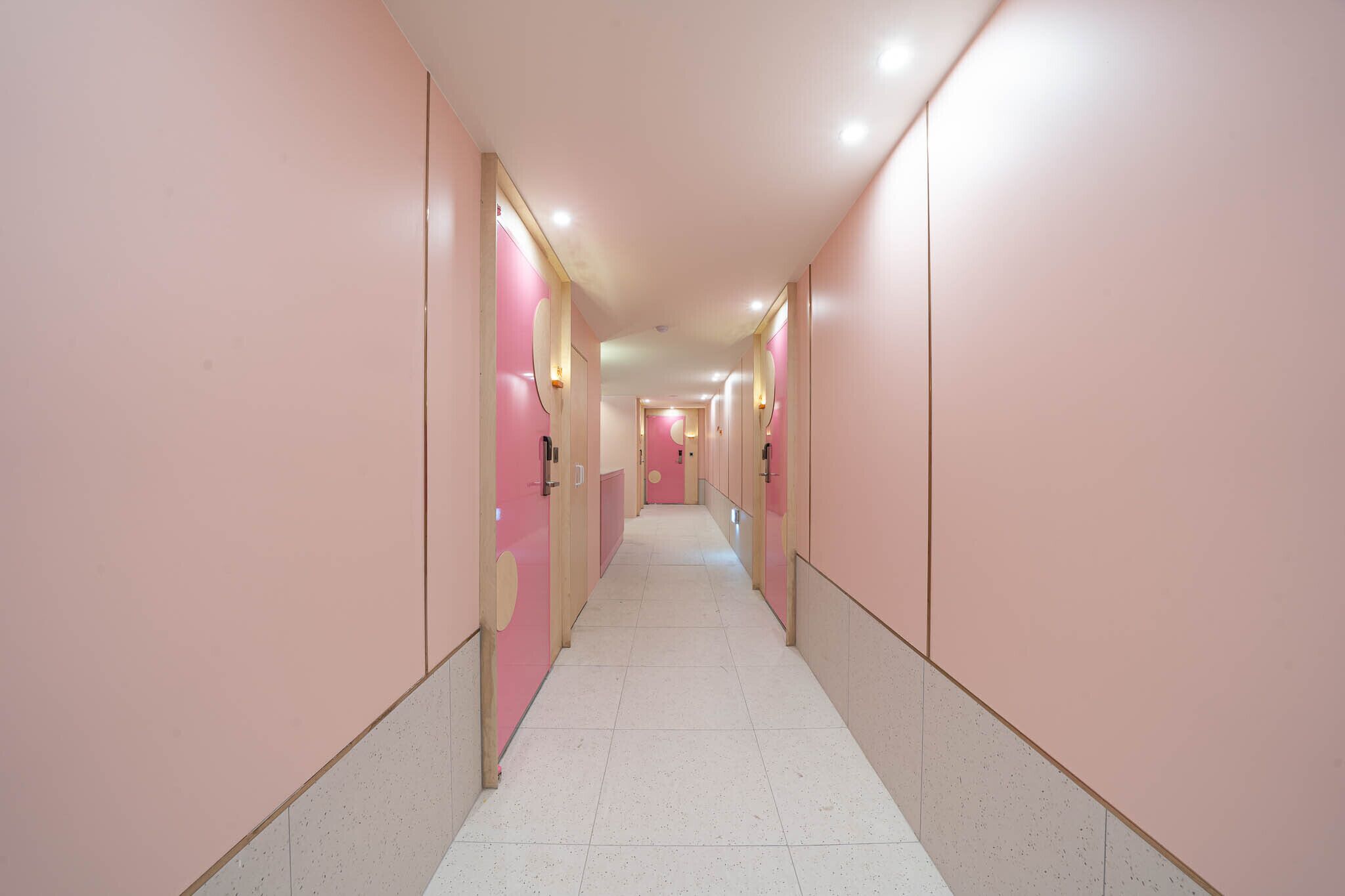 A long, narrow hallway with pink walls and white tiled flooring.