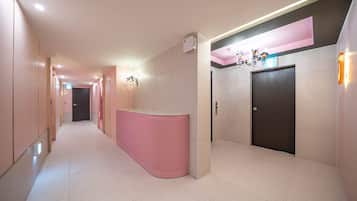 Un pasillo con un mostrador de recepción rosa, una puerta y una lámpara fijada a la pared.