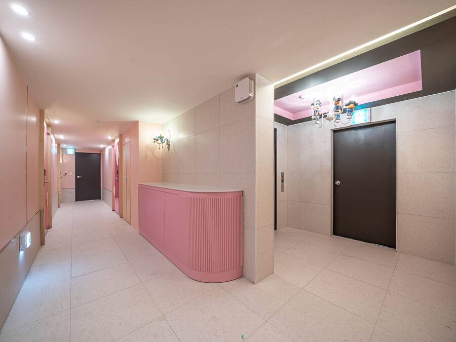 Un pasillo con un mostrador de recepción rosa, una puerta y una lámpara fijada a la pared.