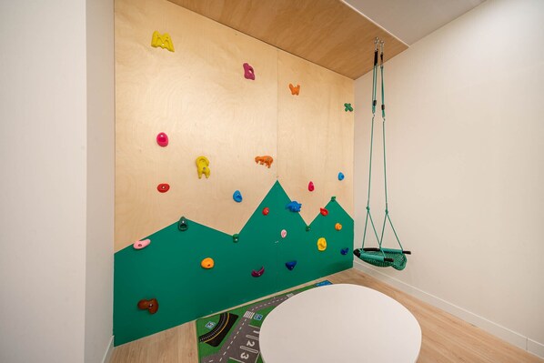 A room with a climbing wall, a hanging swing, and a round table.