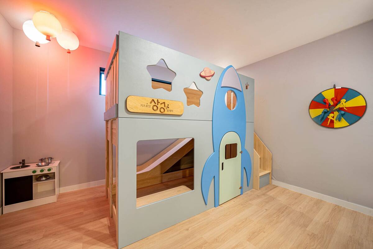 A children's playroom with a rocket play structure, a small kitchen area, and a colorful wall clock.