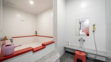 Un baño moderno con azulejos blancos, un área de ducha con azulejos rojos, un taburete pequeño y una tetera rosa sobre la encimera.