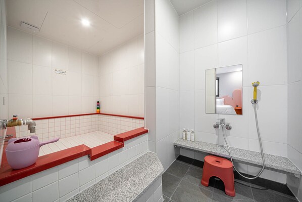 Un baño moderno con azulejos blancos, un área de ducha con azulejos rojos, un taburete pequeño y una tetera rosa sobre la encimera.