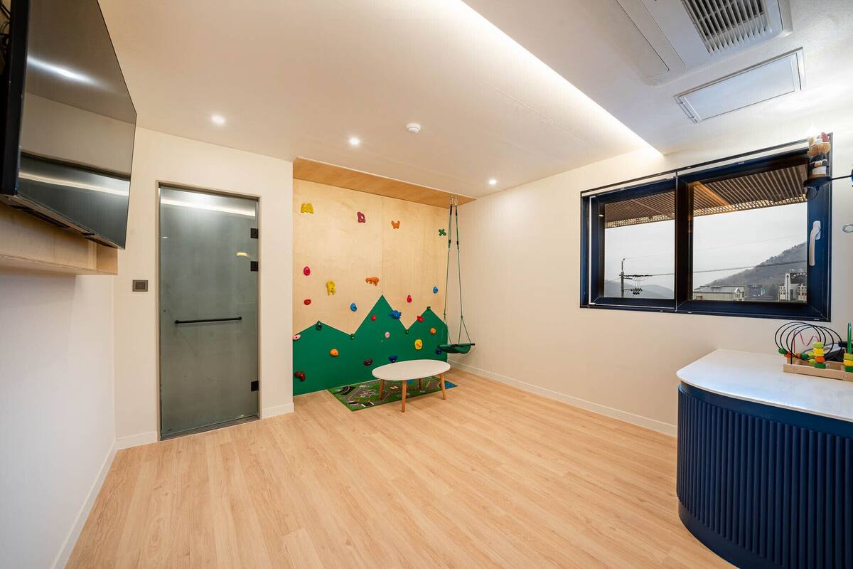 A modern kitchen with a stainless steel range hood, a wooden climbing wall, a small round table, and a window with a view of the city.