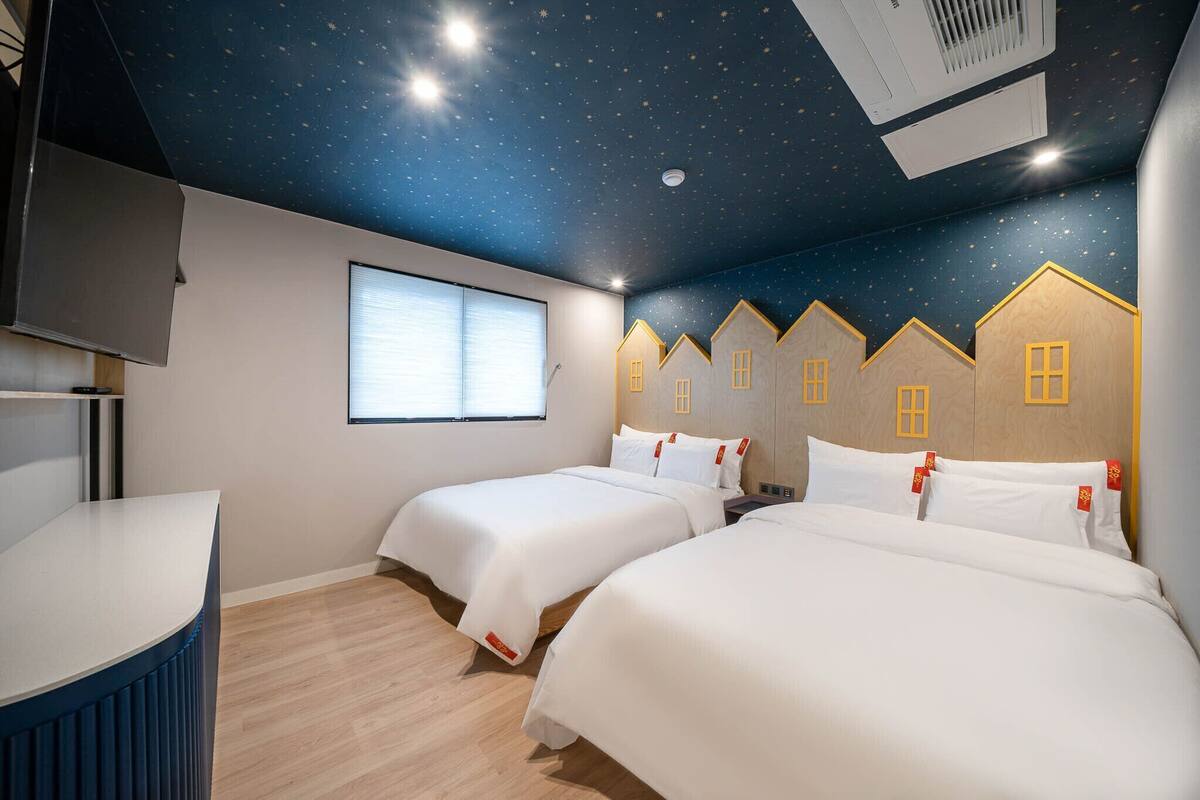 A hotel room with two beds, a starry ceiling, a window, and a wooden wall design.