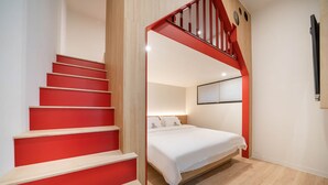 Une chambre avec un escalier rouge, un lit avec une literie blanche et un plancher en bois.