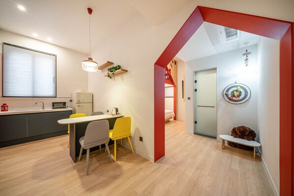Una cocina moderna con comedor, una pared de acento roja y una zona de juegos infantil con un coche de juguete y un oso de peluche.