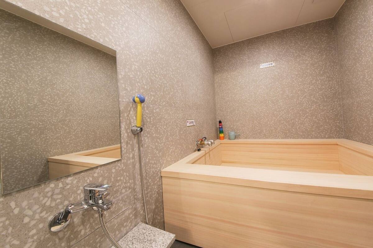 A bathroom with a wooden bathtub, a shower with a handheld showerhead, a sink with a faucet, and a mirror.