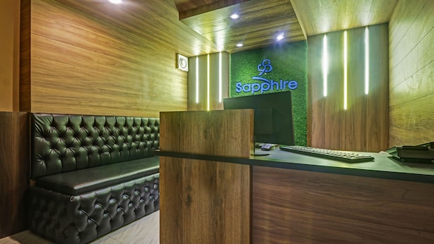 A reception area with a wooden wall, a green wall with a 'Sapphire' sign, a leather sofa, and a reception desk with a computer and keyboard. - Itsy Hotels Sapphire Residency (Ernad)