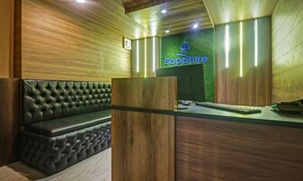 Un área de recepción con pared de madera, pared verde con el letrero 'Sapphire', un sofá de cuero y un mostrador de recepción con una computadora y teclado.