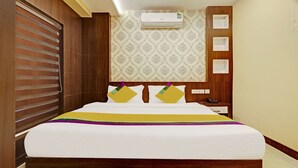 A hotel room with a bed, a nightstand, an air conditioning unit, and a patterned wallpaper. - Itsy Hotels Sapphire Residency (Ernad)