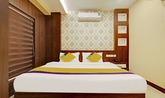 Habitación de hotel con cama, mesita de noche, unidad de aire acondicionado y papel tapiz estampado.
