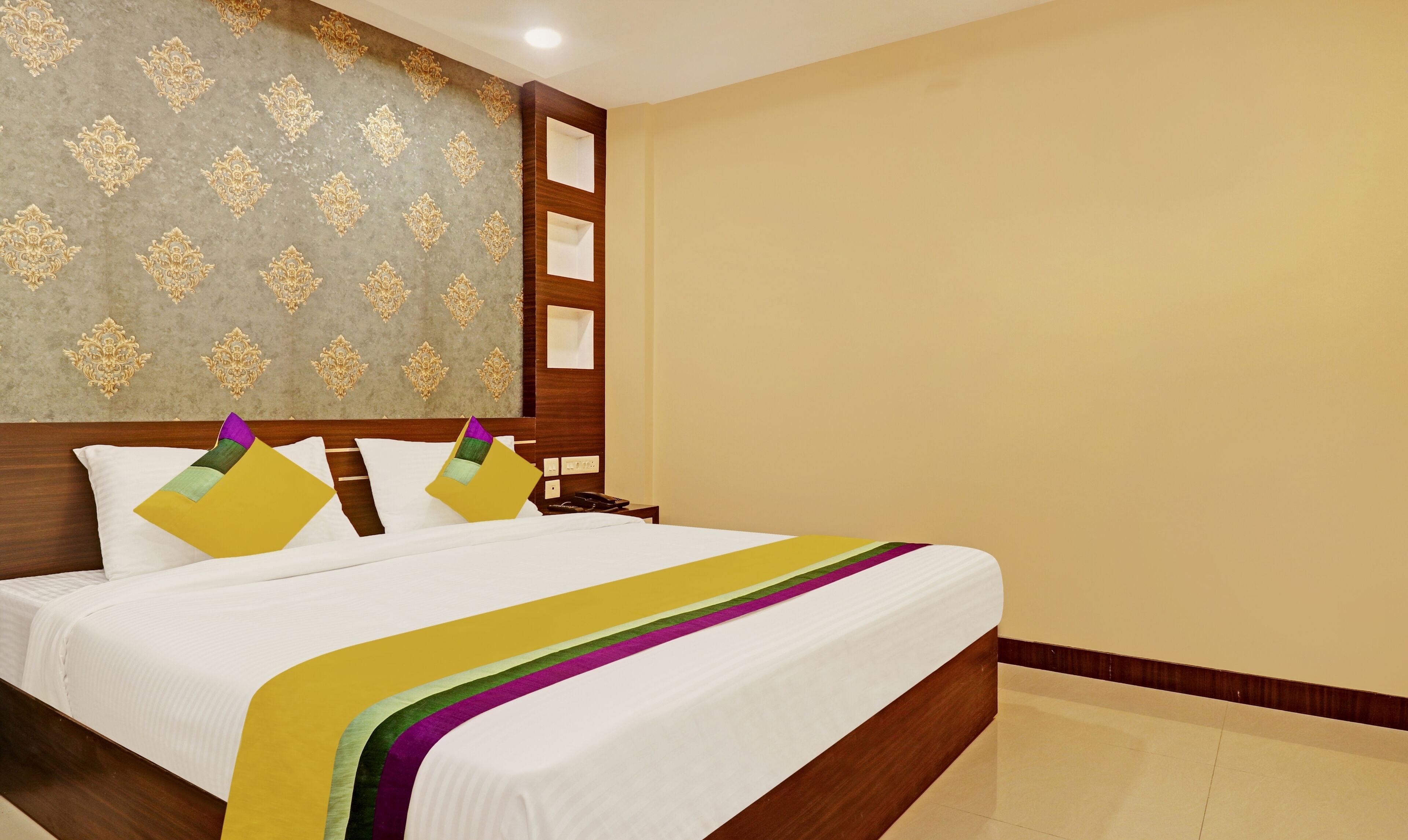 Quarto de hotel com cama, cabeceira de madeira, parede com papel de parede estampado e parede lisa.