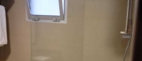 Ducha envuelta en vidrio con cabezal de ducha manual, ventana y una toalla colgada en la pared.