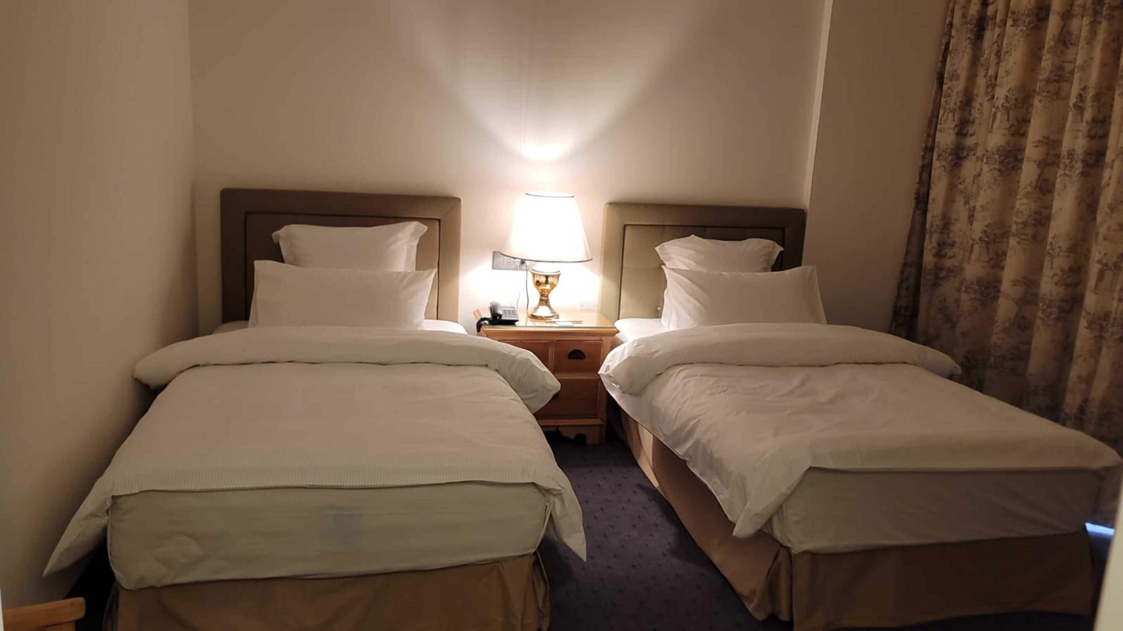A hotel room with two single beds, a nightstand with a lamp, and a telephone.