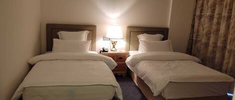 A hotel room with two single beds, a nightstand with a lamp, and a telephone.