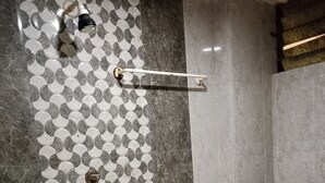 A bathroom with a tiled wall featuring a geometric pattern, a shower area, a toilet, and a pink plastic basin. - Hotel Shiv Sasdan (Veraval)