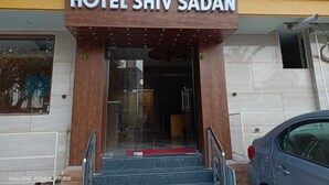 The entrance to Hotel Shiv Sadan with a sign above the door, a red carpet, and a car parked outside. - Hotel Shiv Sasdan (Veraval)