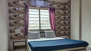 A bedroom with a bed, a window with curtains, and a wall with a floral pattern. - Hotel Shiv Sasdan (Veraval)