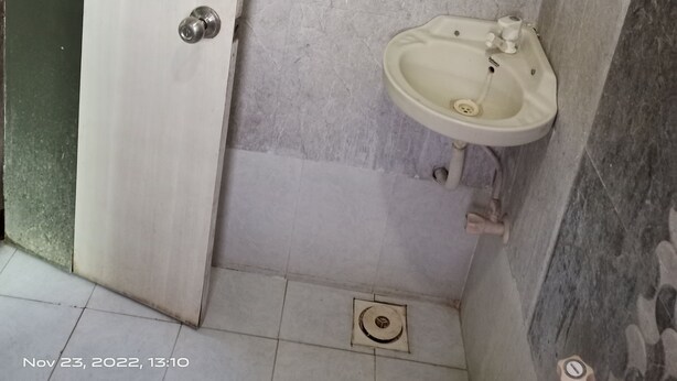 A bathroom with a white door, a sink, and a tiled floor. - Hotel Shiv Sasdan (Veraval)