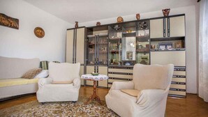 A living room with a sofa, two armchairs, a glass cabinet with decorative items, and a patterned rug.