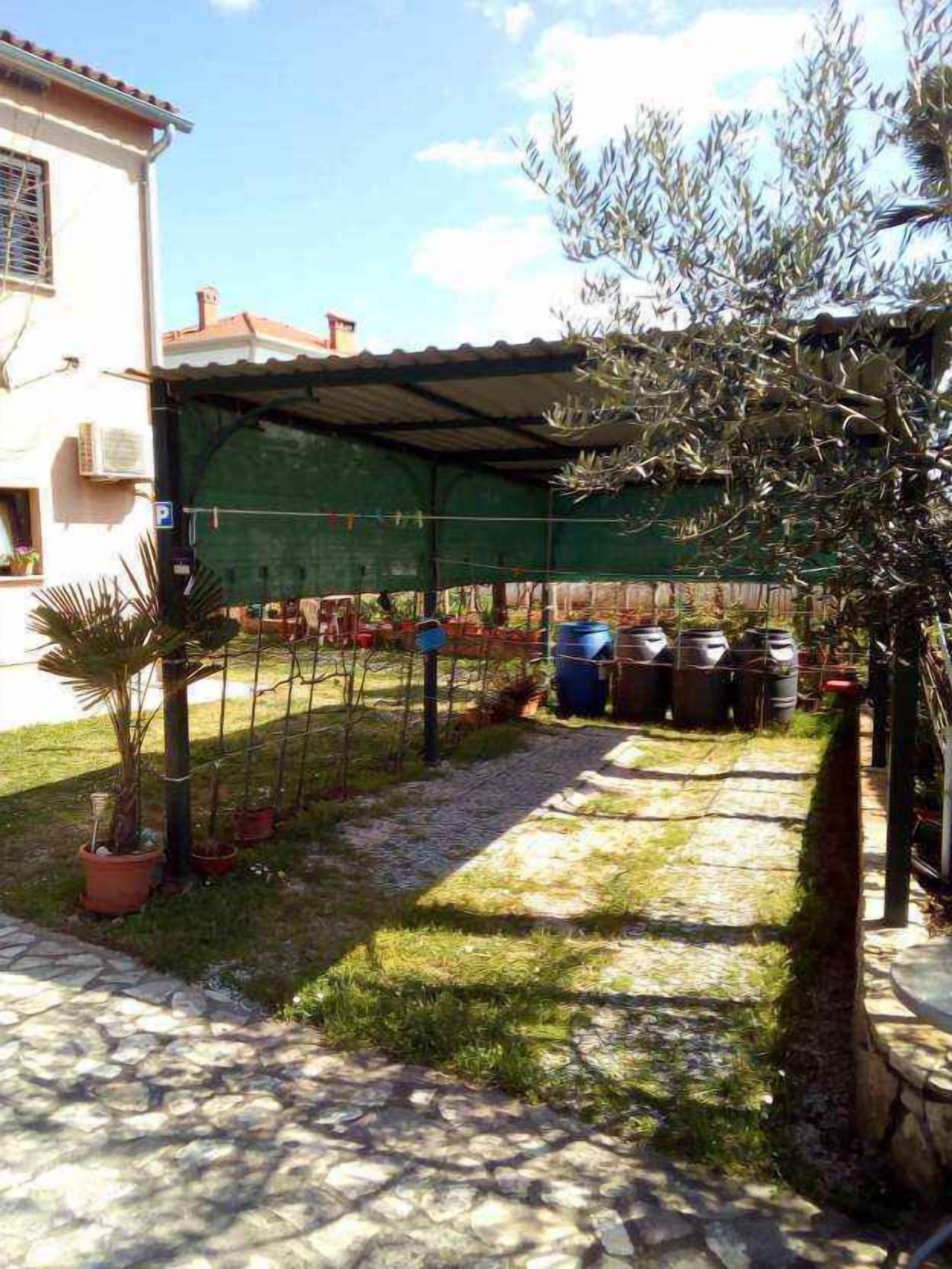 Un patio con sendero de piedra, pérgola verde, plantas en macetas y mobiliario exterior.