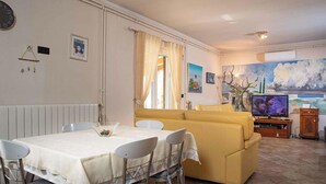 Ein Wohnzimmer mit einer Couch, einem Esstisch mit Stühlen, einem Fernseher und Kunstwerken an den Wänden.
