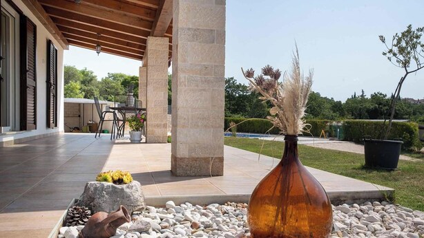 Ein überdachter Patio-Bereich mit Steinpfeilern, Fliesenboden und Gartenmöbeln.
