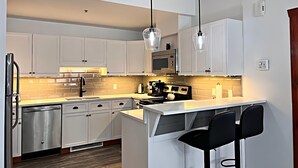 Una cocina moderna con armarios blancos, electrodomésticos de acero inoxidable e iluminación colgante.