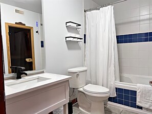 A bathroom with a white sink, toilet, and bathtub. There is a shower curtain and a towel rack. - Les Eaux 227-1 by Escapades Tremblant (Mont-Tremblant)