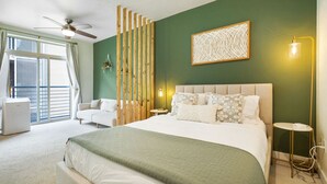 A hotel room with a large bed, a ceiling fan, a wooden partition, a wall-mounted light, and a window with blinds.