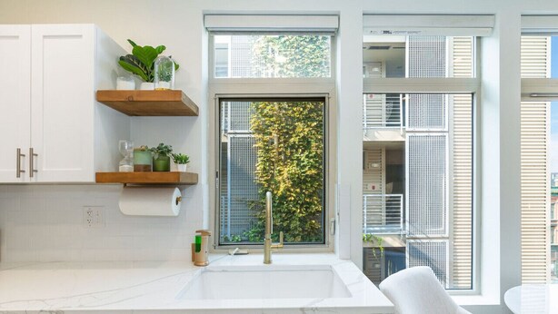 A modern kitchen with white cabinets, a marble countertop, and a window with a view of a tree.