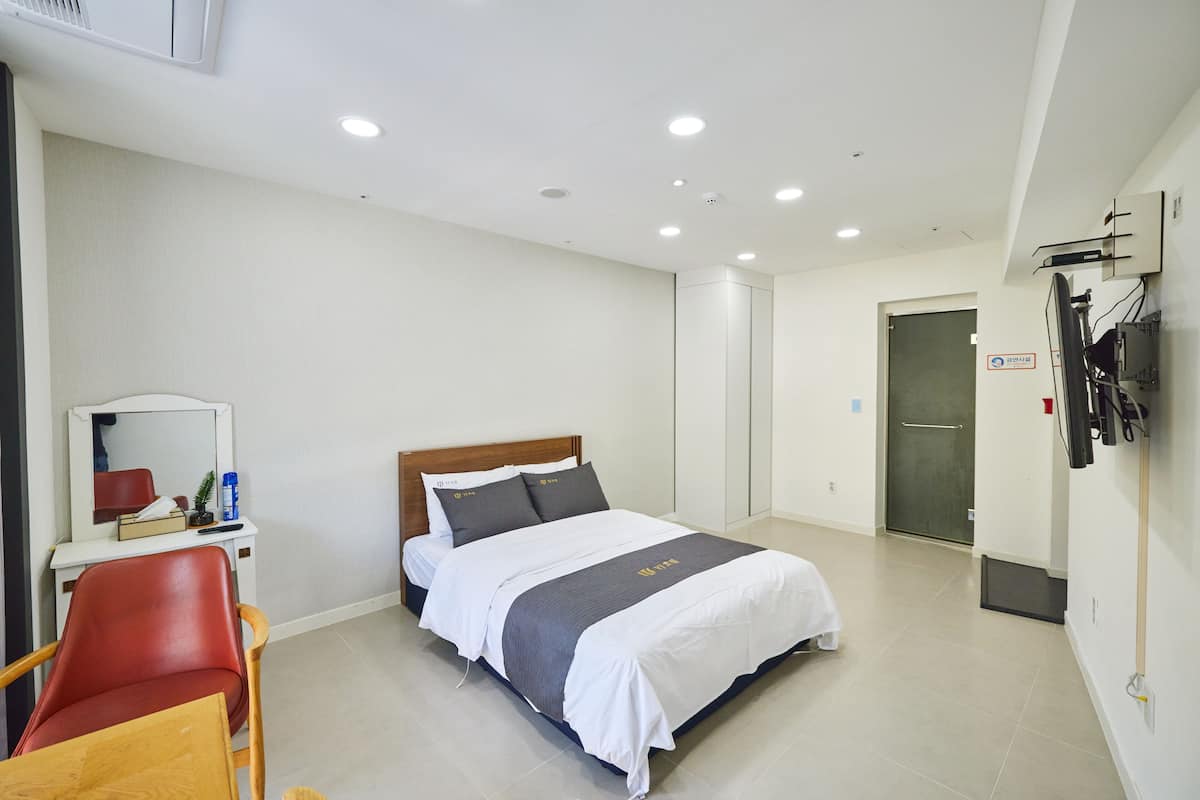 A hotel room with a bed, a desk with a chair, a mirror, and a door.
