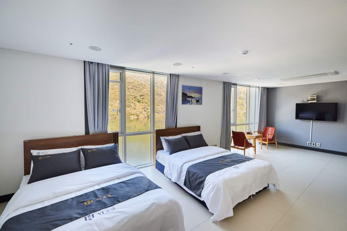 A hotel room with two beds, a TV, a desk, and large windows.