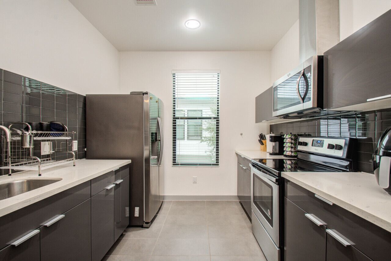 A modern kitchen with stainless steel appliances, a double sink, and a window with blinds.