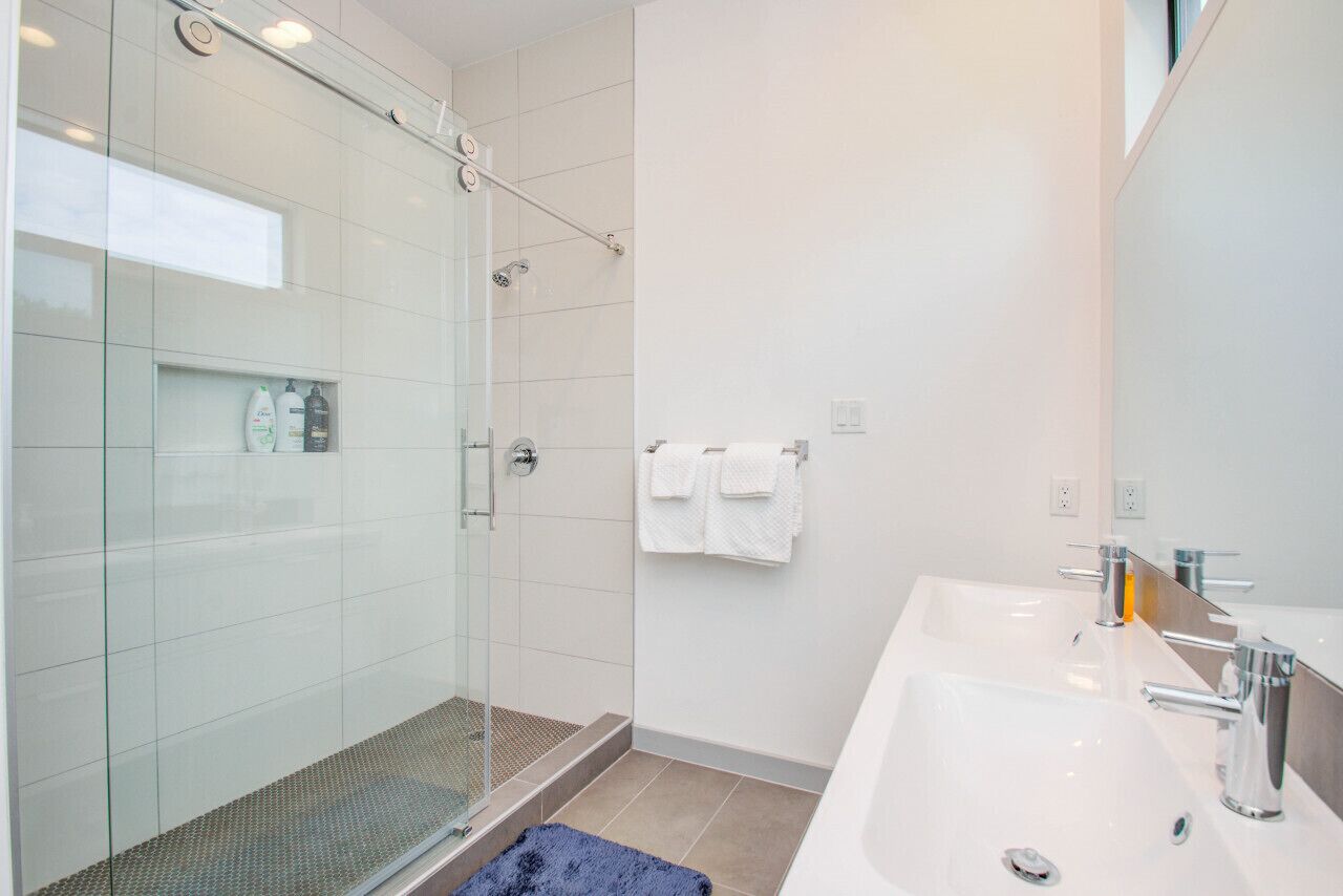 Ein modernes Badezimmer mit einer Duschkabine aus Glas, einem großen Waschbecken und einem Spiegel.