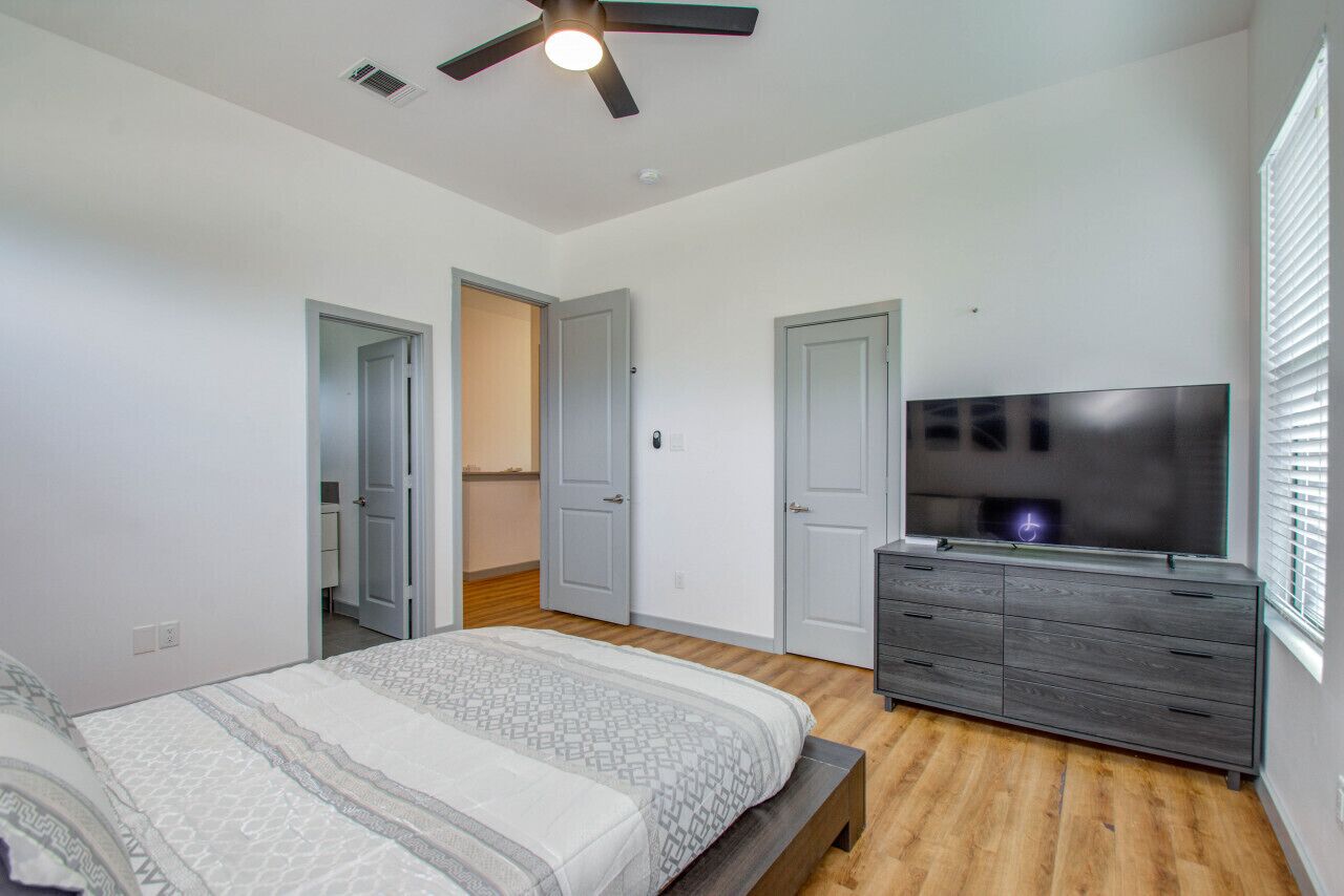 Ein Schlafzimmer mit Bett, Fernseher, Kommode und Deckenventilator.