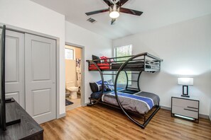 Un dormitorio pequeño con una cama litera, un ventilador de techo, una mesita de noche con lámpara y suelo de madera.
