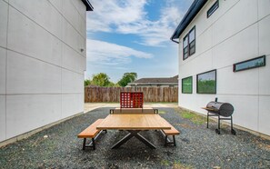 Una mesa de picnic con bancos en un patio, con una valla de madera y una parrilla.