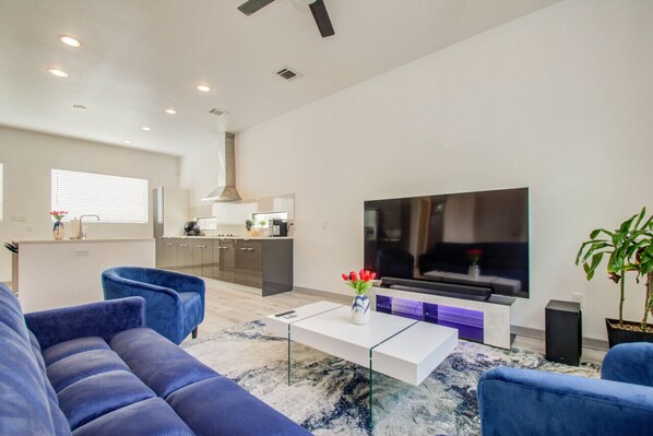 Una sala de estar moderna con un televisor de pantalla plana grande, una mesa de centro blanca y sofás azules.