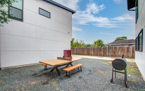 Un patio con mesa de picnic y banco, una parrilla y una valla de madera al fondo.