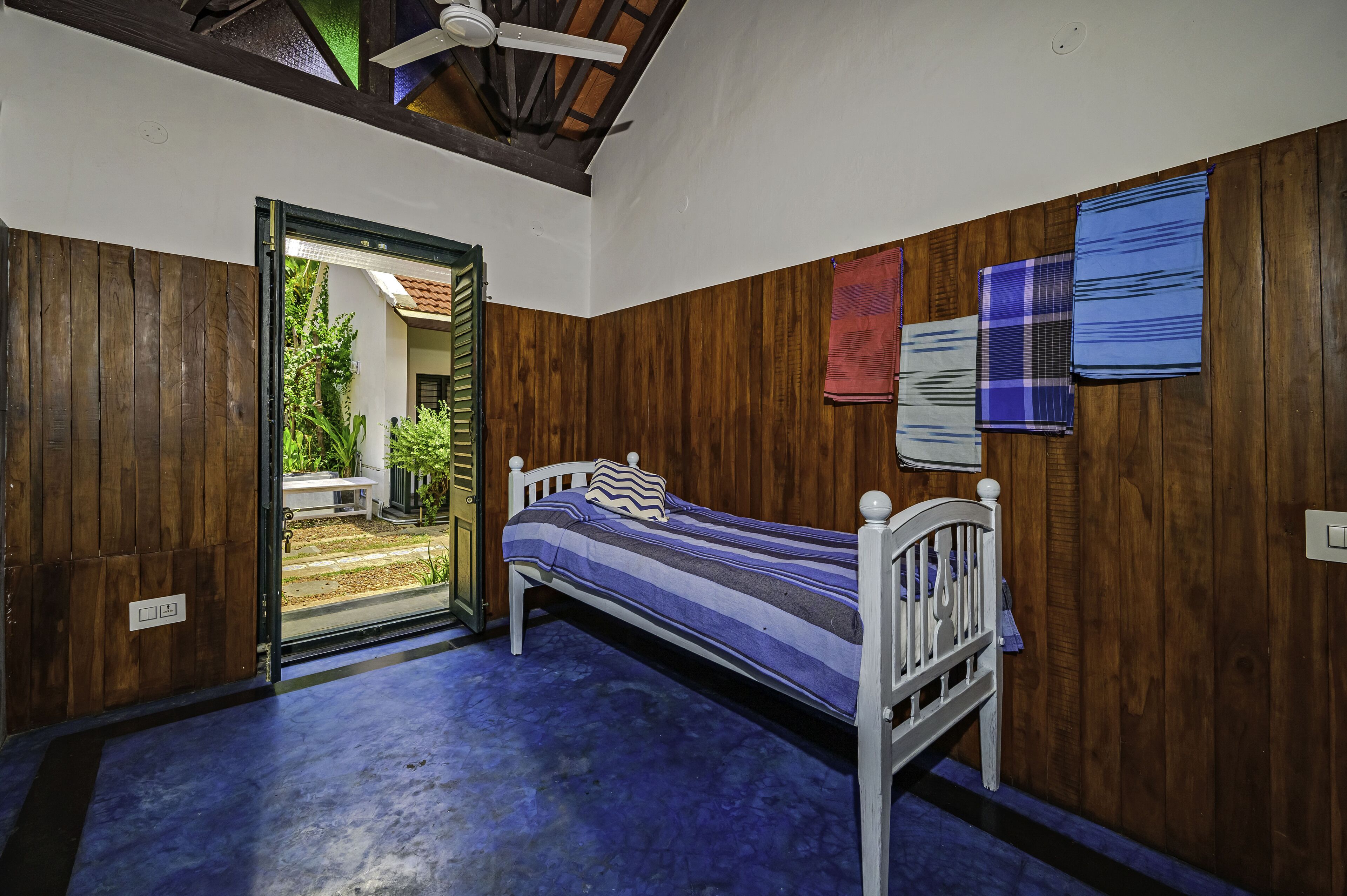 A bedroom with a wooden floor, a bed with a striped bedspread, and a ceiling fan.
