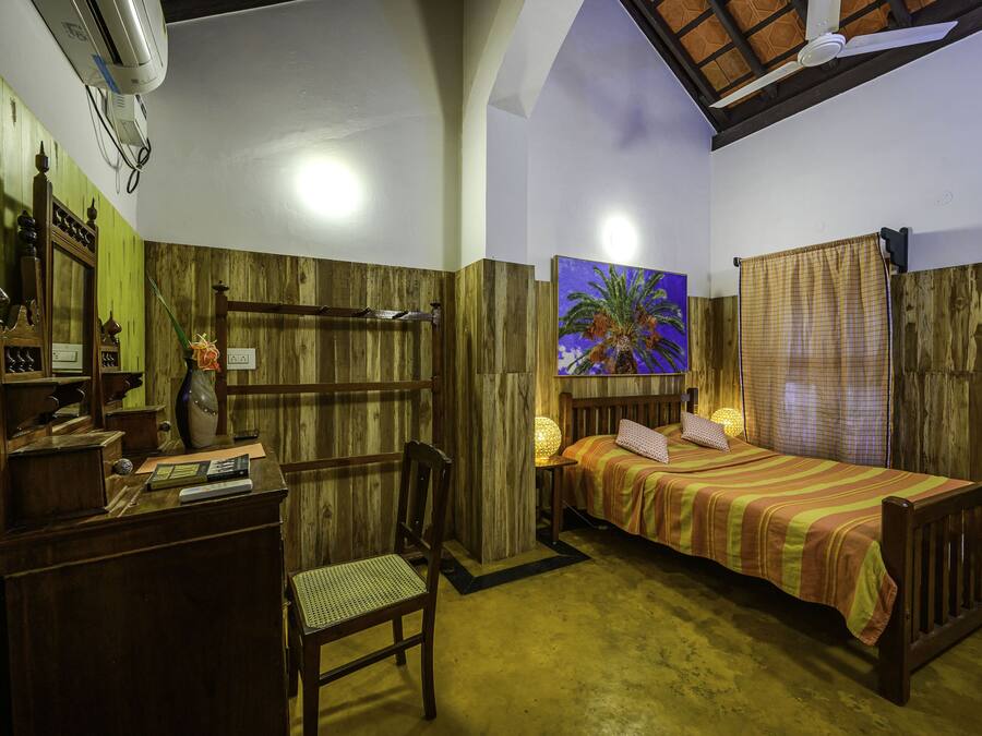 Una habitación con cama, escritorio, silla y un cuadro de una palmera.